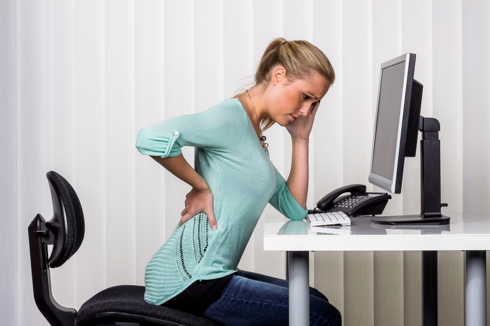 a woman sitting at a desk and has pain in her back. photo icon for proper posture at work in the office.